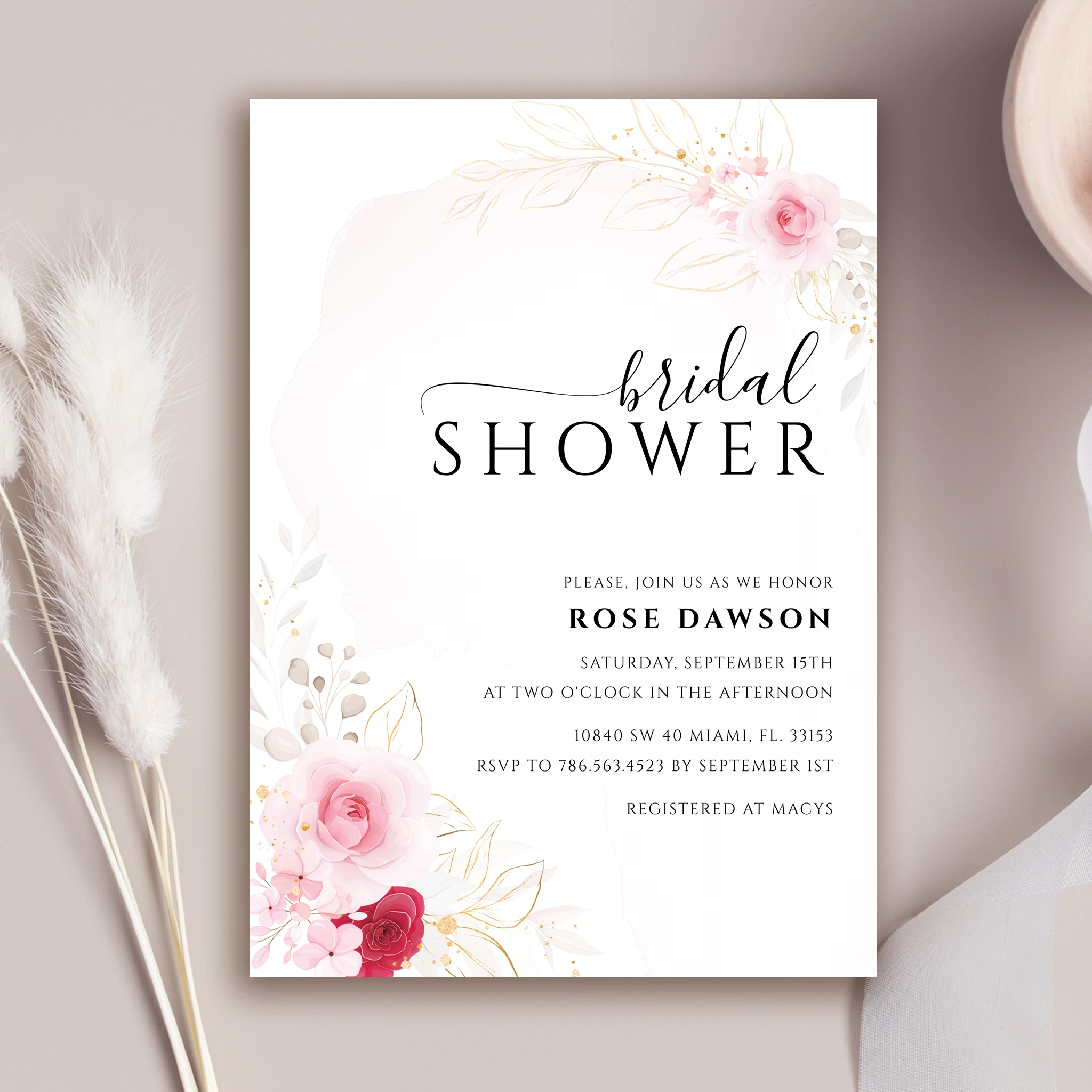 Elegant bridal shower invitation adorned with delicate pink-toned flowers accented with gold details, complemented by exquisite calligraphy.